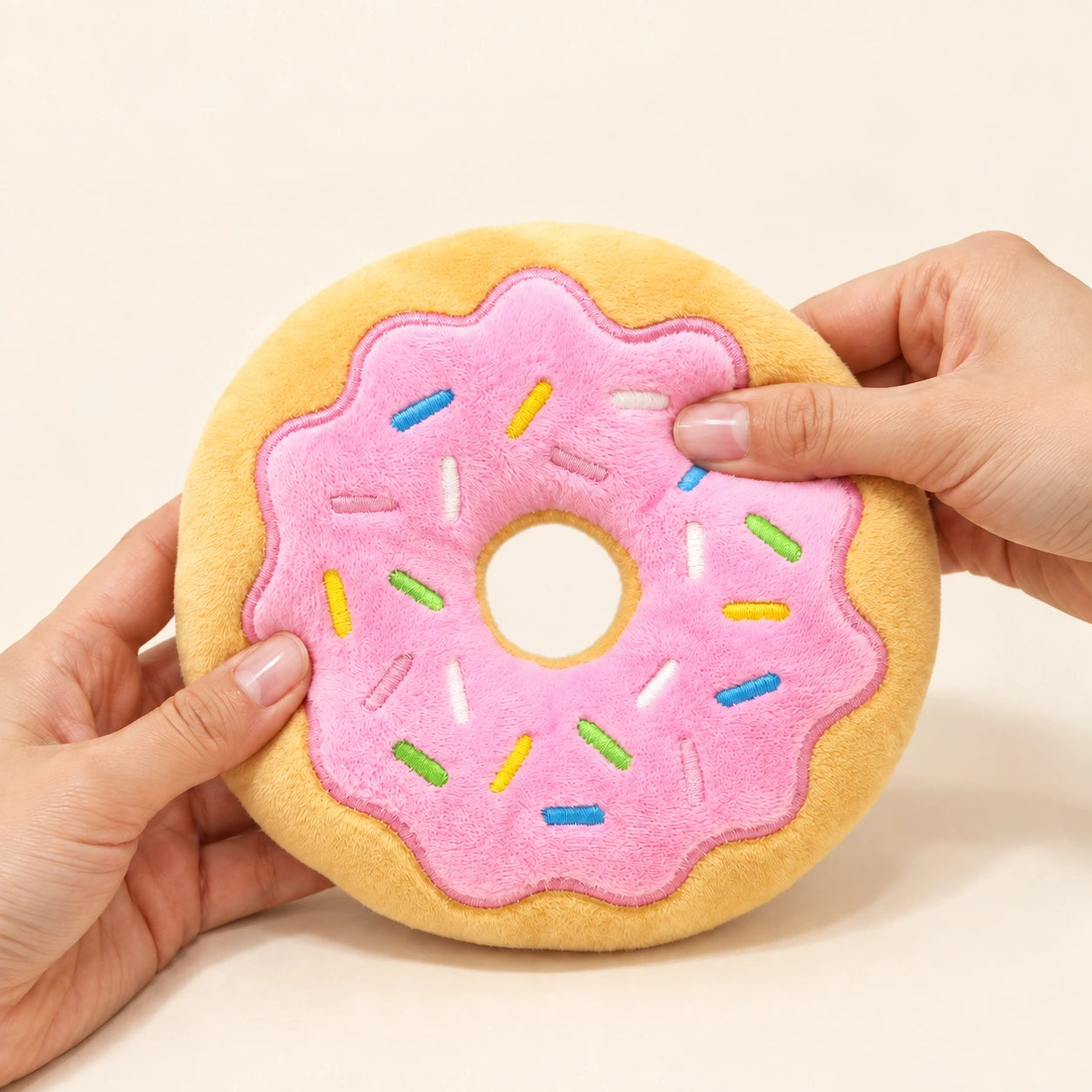 Hands gently pressing the pink stuffed donut to demonstrate squeaky play