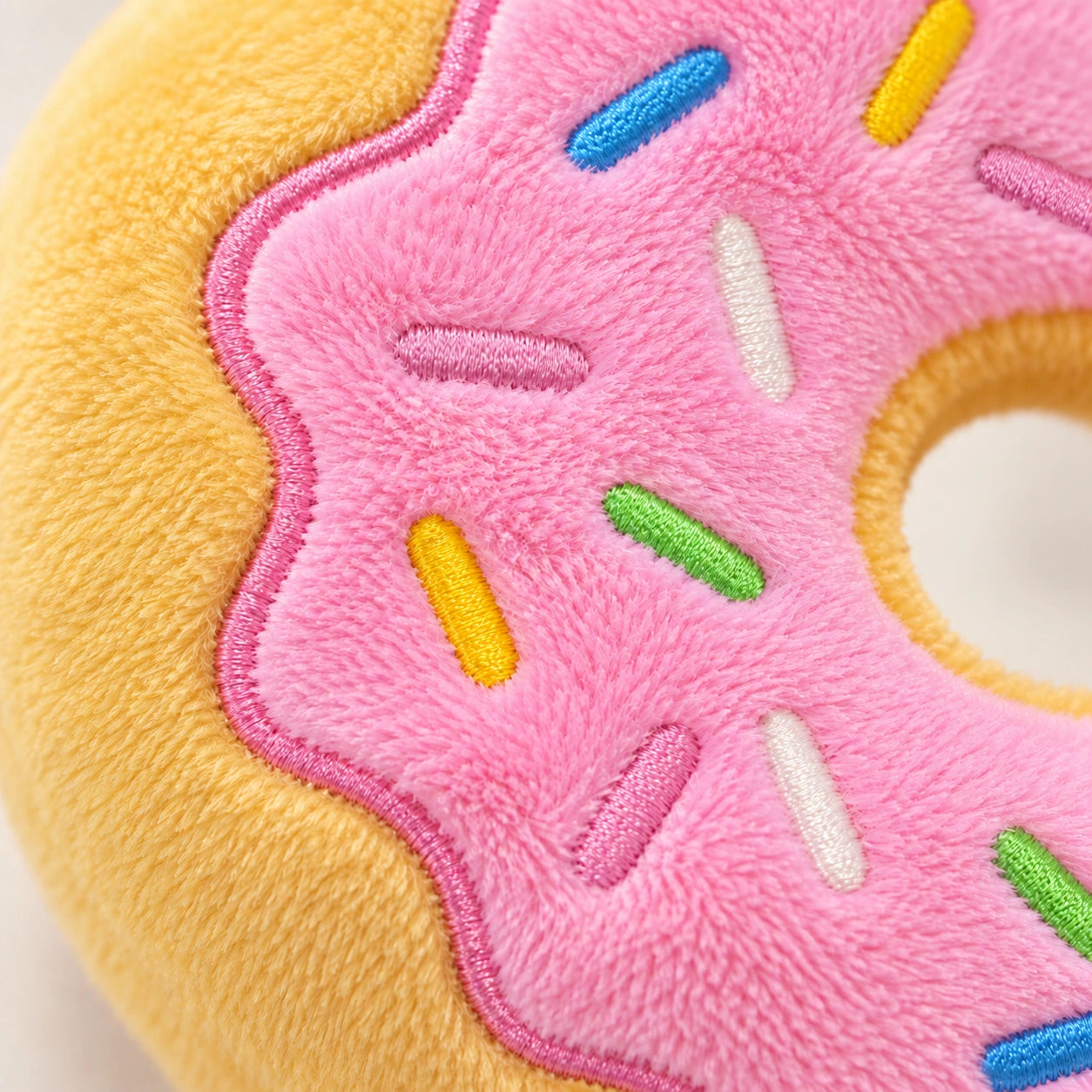 Close-up of pink plush icing, stitched sprinkles and the golden-yellow fabric edge