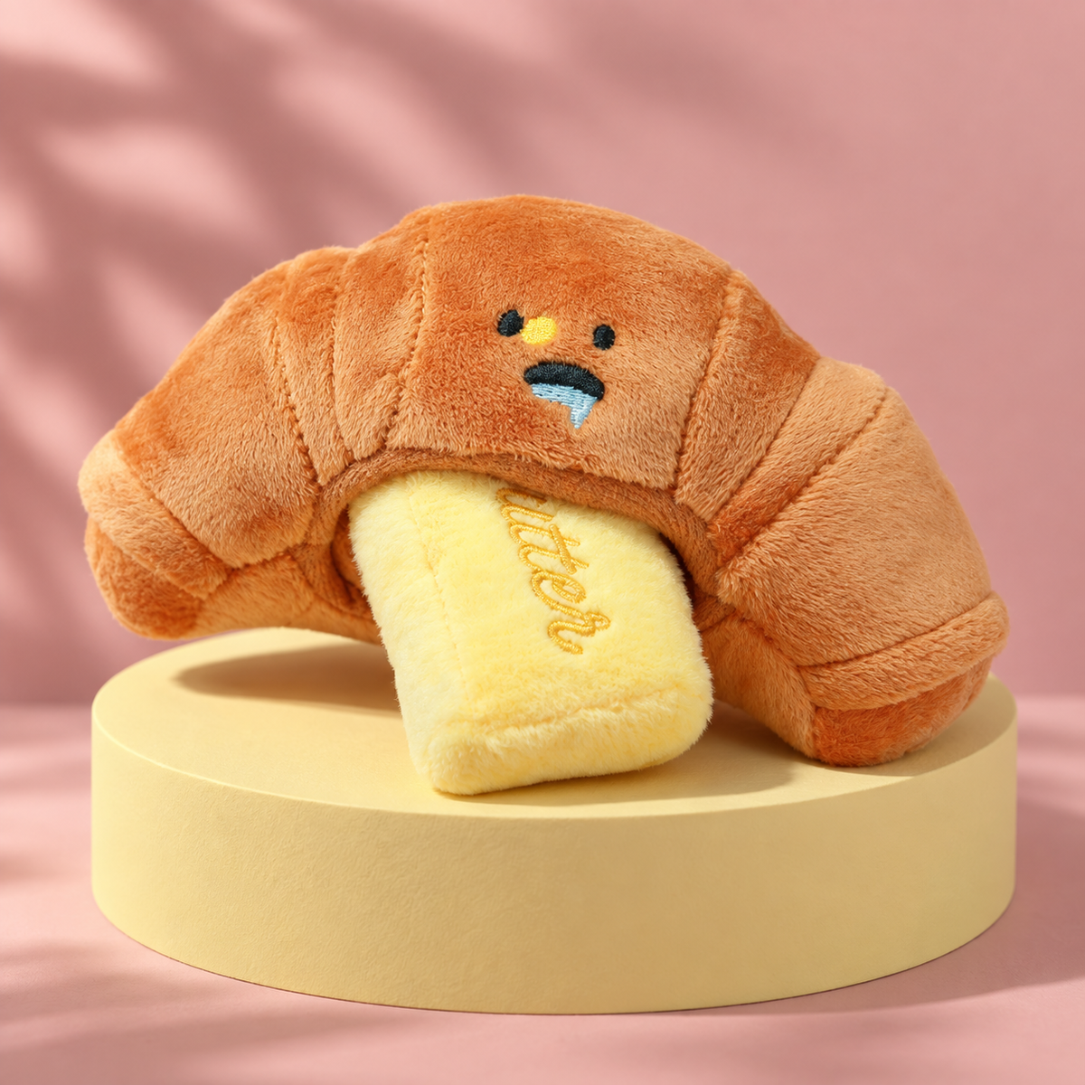 Croissant plush toy with yellow Butter insert on a butter plinth.