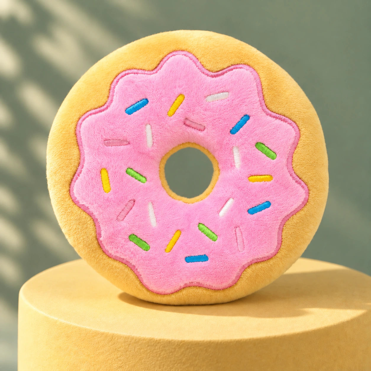 Pink plush donut on a butter-yellow plinth